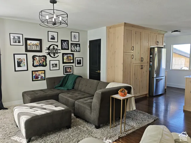 Wood-finish flooring, custom light-toned wood cabinetry, stainless steel refrigerator, black interior door with brass hardware, and geometric metal pendant lighting