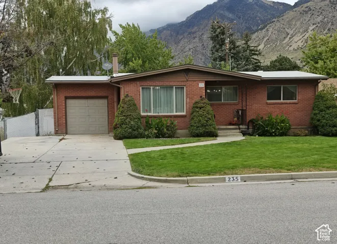 Single-story brick exterior featuring a low-slope roof, an attached garage, a concrete driveway, and mountain scenery
