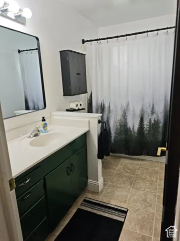 Bathroom featuring a vanity with an integrated basin, a wall-mounted medicine cabinet, a rectangular mirror with a metal frame, a dual-light fixture, and tile flooring