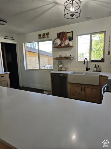Kitchen featuring solid-surface countertops, wood cabinetry, a dual-basin farmhouse sink with matte black fixture, hexagonal tile backsplash, and decorative wall-mounted shelving