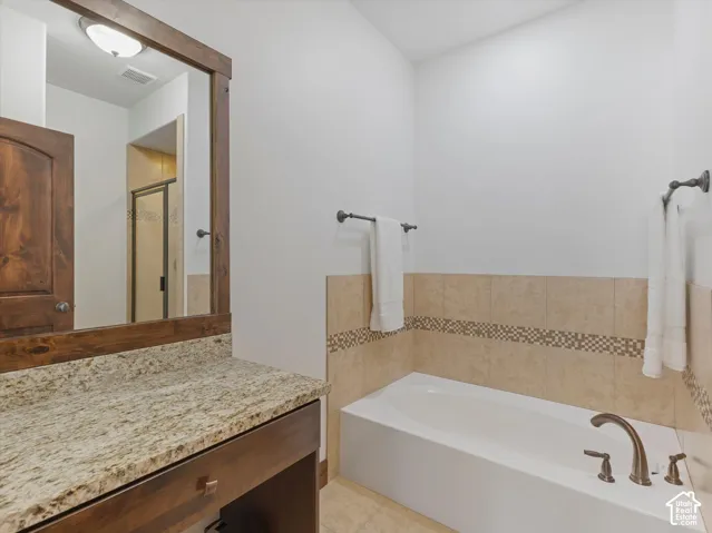 Bathroom vanity featuring a stone-look countertop, wood-finish cabinetry, and a wood-framed mirror, complemented by a drop-in bathtub with tile surround and oil-rubbed bronze fixtures