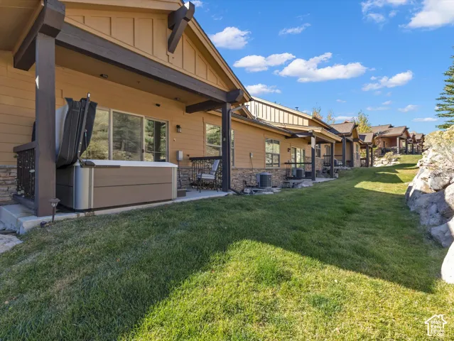 Covered patio featuring stone veneer accents, wood-style siding, heavy timber structural supports, and a built-in jetted spa, set against a tiered landscape with natural rock formations