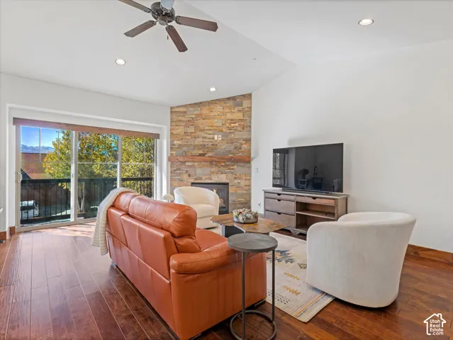 Vaulted ceiling with recessed lighting, stone-clad fireplace with timber mantel, wood-finish flooring, and sliding glass doors