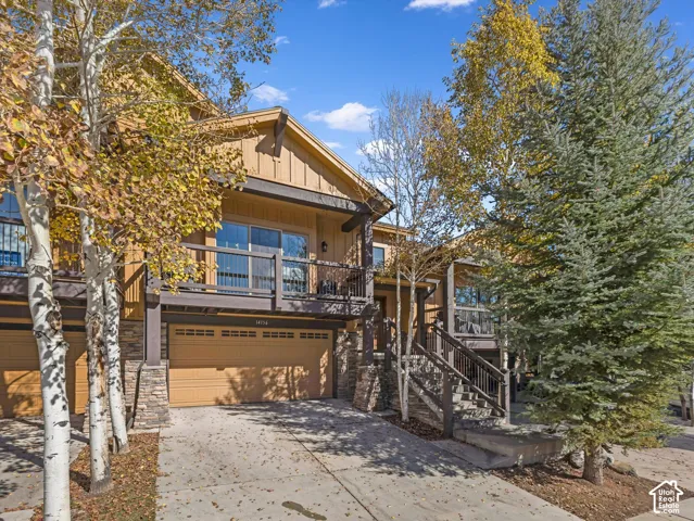 Multi-level exterior featuring vertical wood siding, stone veneer accents, an integrated two-car garage, and a raised wooden balcony with decorative metal railing