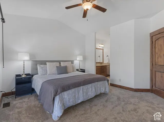 Vaulted ceilings, neutral carpeting, ceiling fan with light fixture, stained wood door, and vanity with stone-style countertop