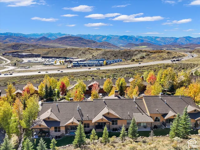 Multi-unit residential structure with dark shingled multi-pitch roofing, exterior stone cladding, and wood-finish siding, set against a mountainous backdrop