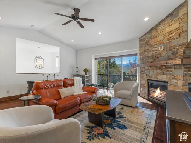 Living area featuring wood-finish flooring, a full-height stone fireplace with a timber mantel, vaulted ceilings, recessed lighting, and a glass sliding door