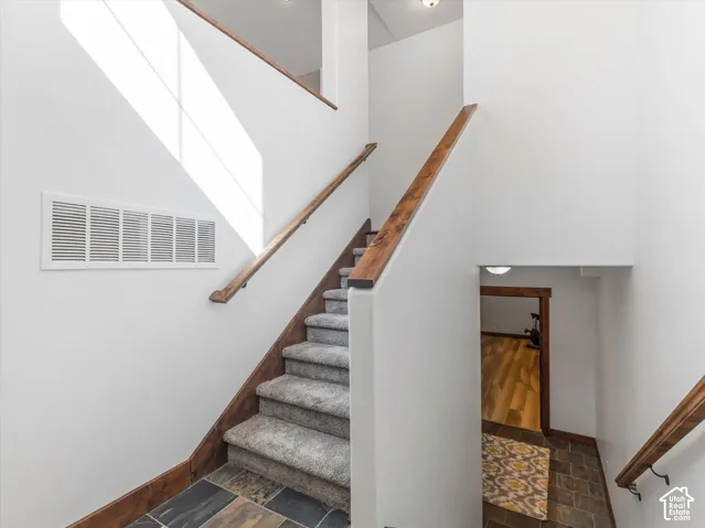 Staircase featuring carpeted steps, wood-finish handrails, and multi-tonal stone-style tile flooring