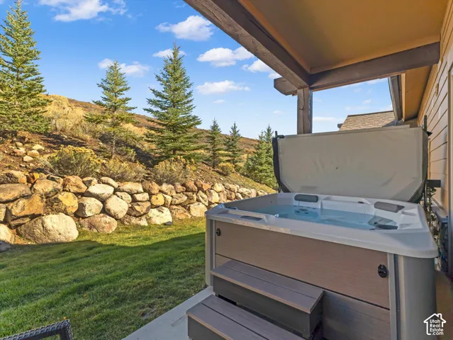 Covered patio featuring an integrated hot tub with matching steps, tiered rock retaining wall, and landscaped grounds
