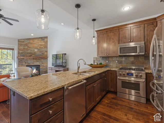 Kitchen featuring dark wood cabinetry, stone-surface countertops, stainless steel appliances, glass pendant lighting, and wood-finish flooring