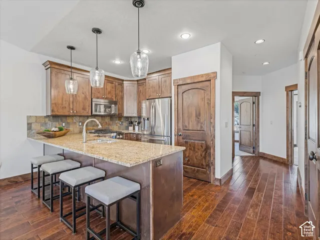 Kitchen featuring a stone-topped island with an integrated stainless steel sink, custom wood cabinetry, wood-finish flooring, and pendant lighting