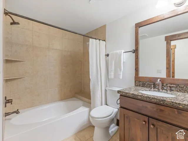 Bathroom featuring a stone-topped vanity with wood cabinetry, a framed mirror, and a tile-surround bathtub with integrated shelving
