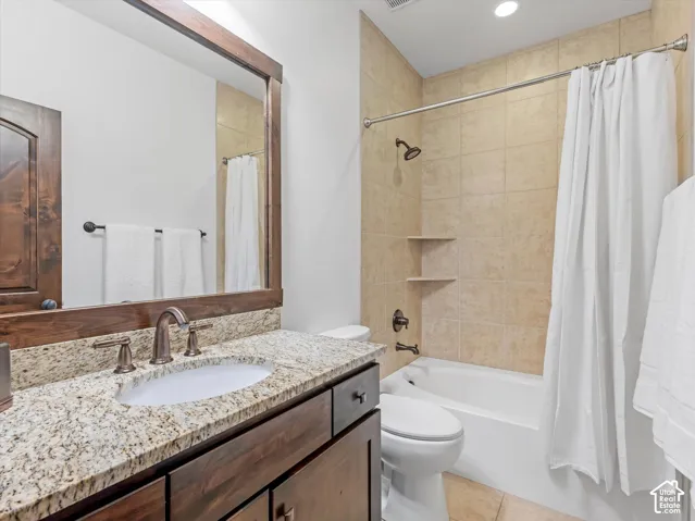 Bathroom featuring a vanity with stone-finish countertop, undermount sink, and wood-finish cabinetry, paired with a shower-tub combination featuring tiled surround and integrated shelving