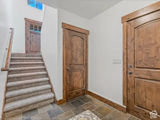 Interior space featuring multi-tonal slate tile flooring, stained wood interior doors with matching thick-profile door casings, carpeted staircase with a wood handrail, and high-reaching ceilings