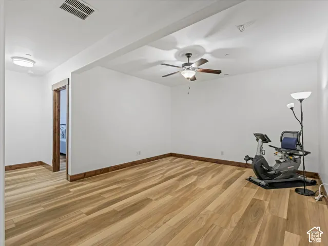 Spacious room featuring wood-finish flooring, natural wood door casing, a ceiling fan with integrated lighting, and a neutral color palette