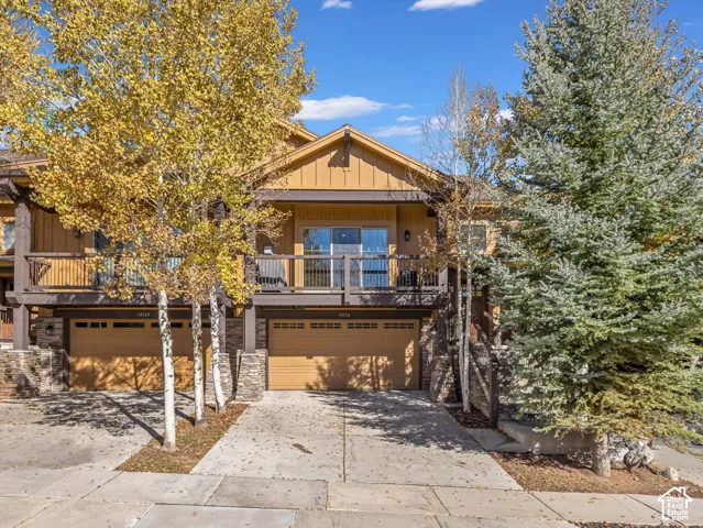 Multi-level exterior featuring vertical wood-style siding, stone masonry accents, an attached two-car garage, and an upper-level balcony with metal railings