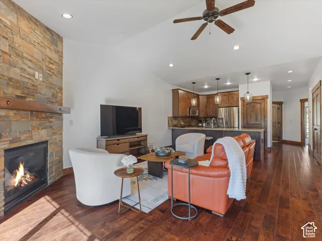 Floor-to-ceiling stone fireplace with a prominent timber mantel, wood-finish flooring, recessed lighting, and cabinetry with stone countertops
