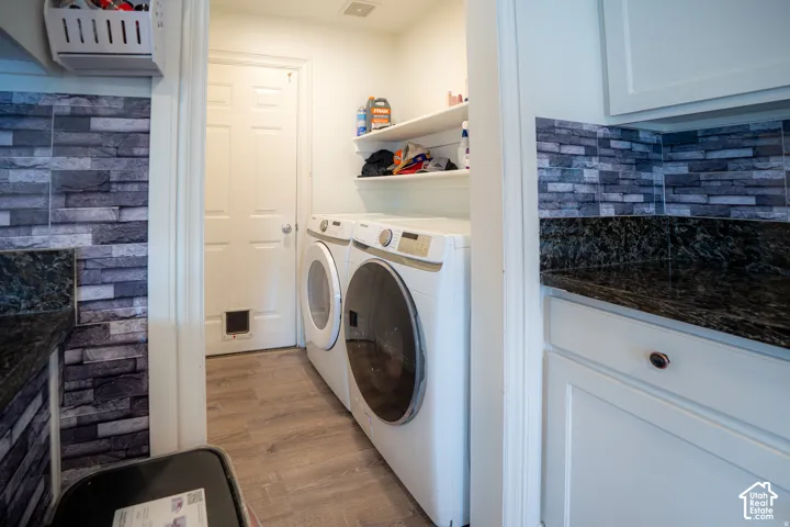 Laundry room featuring stone-textured tile backsplash, dark stone-finish countertops, shaker-style cabinetry, wood-finish flooring, and built-in shelving