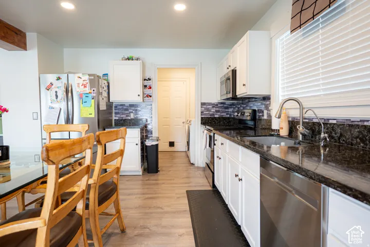 Kitchen featuring white cabinetry, dark stone countertops, stainless steel appliances, a mosaic tile backsplash, and wood-finish flooring