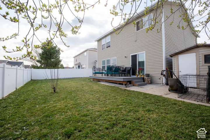 Rear exterior featuring vinyl siding, an elevated wood deck, a concrete patio, and a fenced backyard with an exterior storage shed