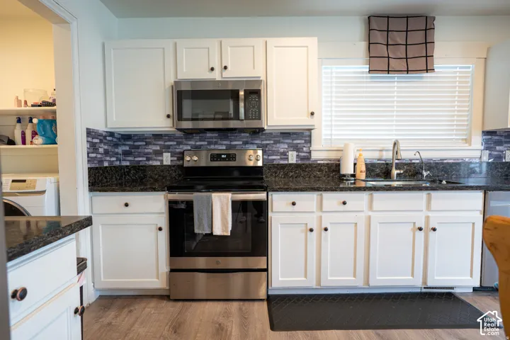 Kitchen featuring white shaker-style cabinetry, stone-finish countertops, stainless steel appliances, multi-tonal tile backsplash, and wood-finish flooring
