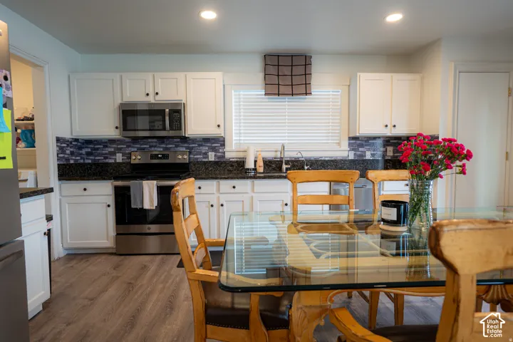 Kitchen featuring white cabinetry, dark stone countertops, a mosaic tile backsplash, stainless steel appliances, and wood-finish flooring