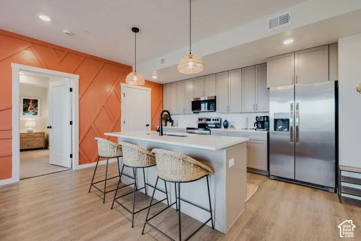 Kitchen featuring a central island with a solid-surface countertop, shaker-style cabinetry, stainless steel appliances, wood-finish flooring, and decorative wall paneling