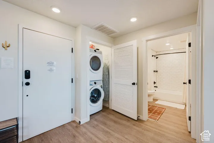 Stacked laundry units, wood-finish flooring, recessed lighting, and a bathroom featuring white subway tile wall surround