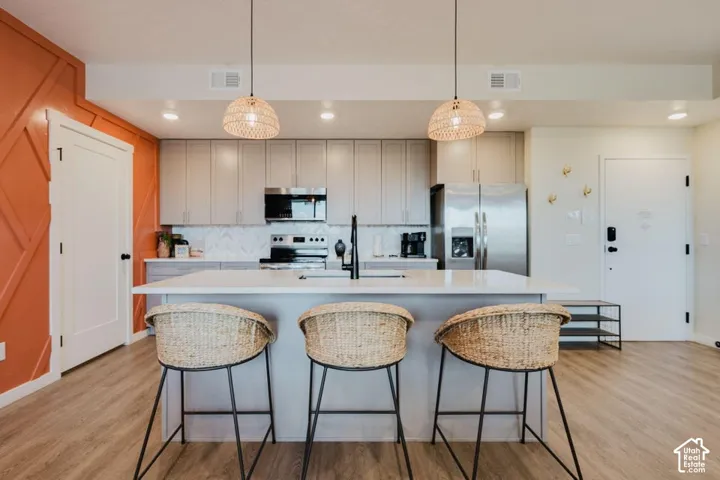 Kitchen featuring a central island with a solid-surface countertop, shaker-style cabinetry, stainless steel appliances, herringbone-patterned tile backsplash, and woven pendant lighting