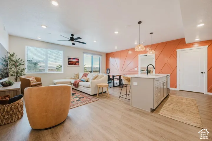Open-concept area featuring wood-finish flooring, a kitchen island with stone-finish countertops, recessed lighting, a modern ceiling fan, and a decorative paneled accent wall