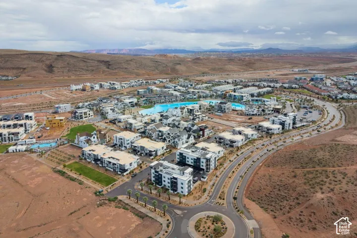 Aerial view of a residential community featuring a large turquoise recreational lagoon, paved streets, manicured green spaces, and a mountainous desert backdrop