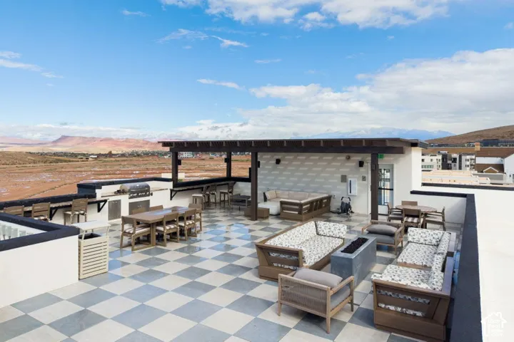 Rooftop terrace featuring a checkered tile floor, built-in outdoor kitchen with integrated grill, overhead timber-frame pergola, and mountain horizon scenery
