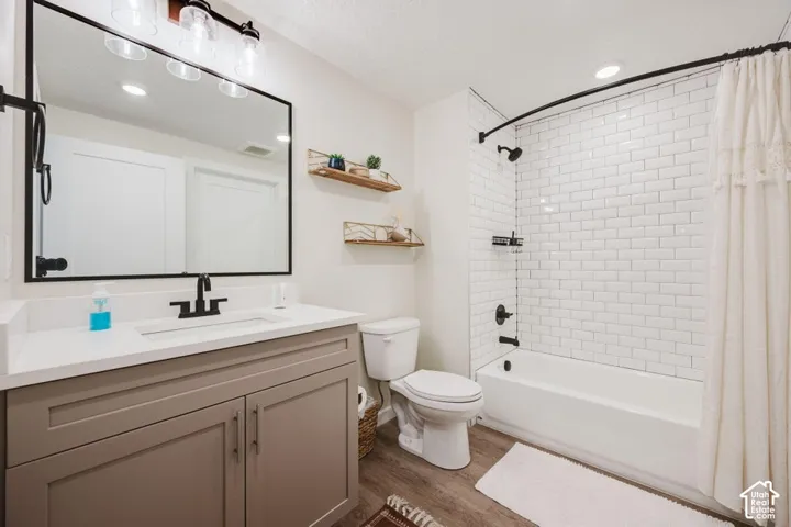 Bathroom featuring a vanity with a white countertop and matte black fixtures, rectangular mirror with a black frame, tub-shower combination with white subway tile surround, and wood-finish flooring