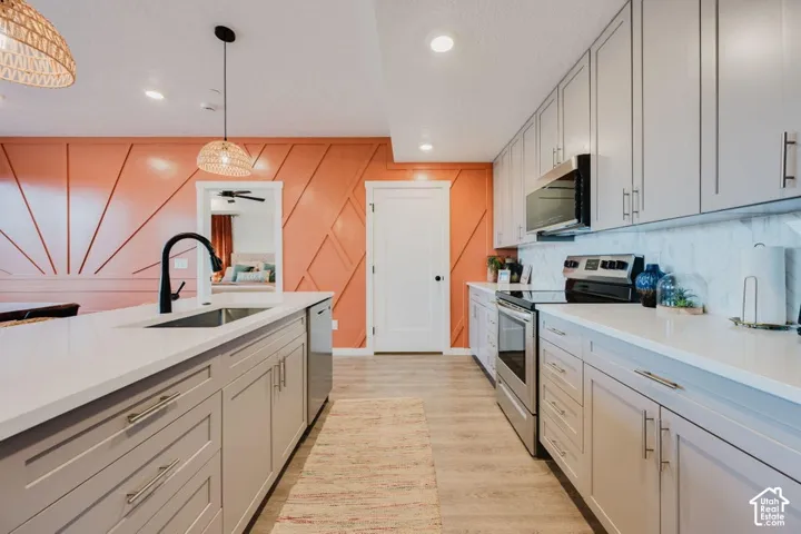 Kitchen featuring light gray shaker-style cabinetry, white quartz countertops, wood-finish flooring, a matte black high-arch faucet, and an accent wall with geometric wood molding