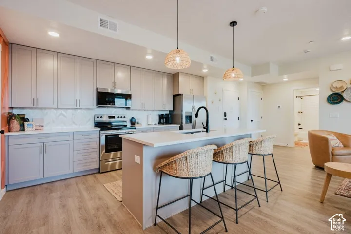 Kitchen featuring shaker-style cabinetry, a central island with quartz countertops, stainless steel appliances, a chevron-patterned tile backsplash, and overhead pendant lighting