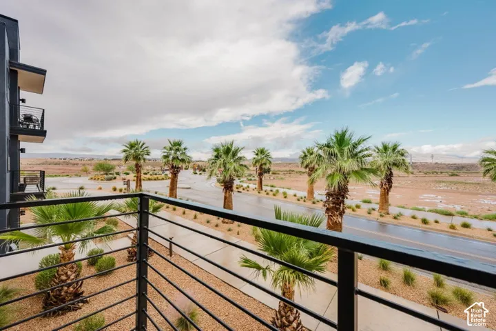 Covered balcony featuring black metal railings, desert landscaping, palm trees, and an asphalt street
