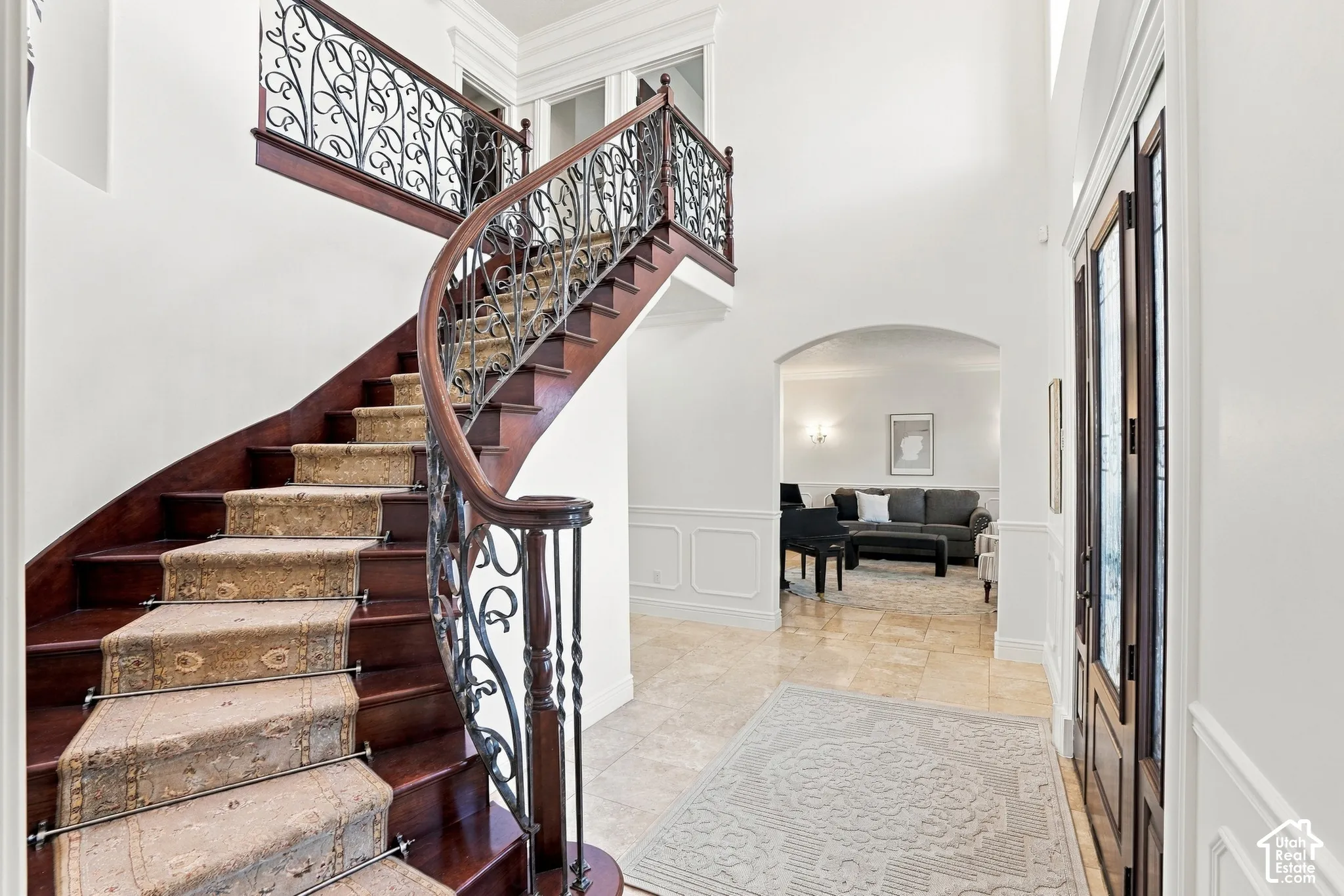 Grand foyer featuring a curved staircase with wood treads, intricate iron balusters, and wainscoting, complemented by stone-finish tile flooring