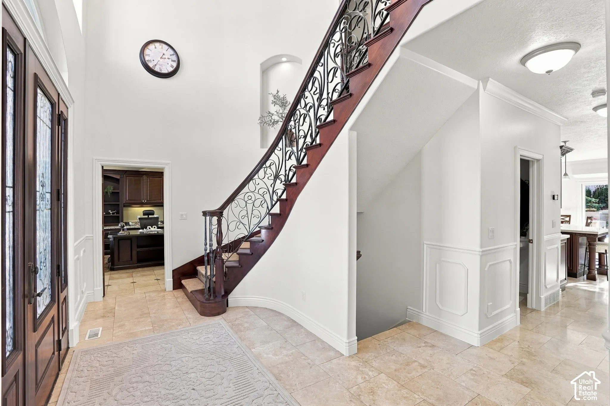 Foyer featuring vaulted ceilings, stone flooring, decorative wainscoting, an arched wall niche, and a sweeping staircase with ornate metal railings and a wood handrail