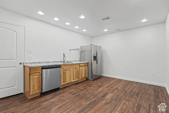 Kitchen area featuring natural-finish wood cabinetry, stone-patterned countertops, stainless steel appliances, and wood-finish flooring with recessed ceiling lighting