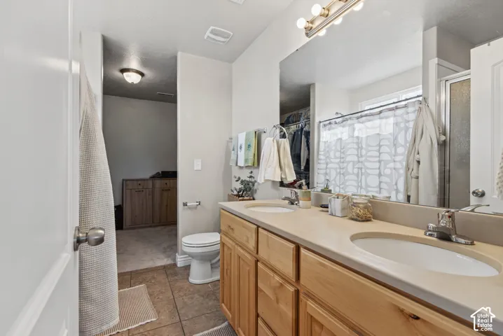 Bathroom vanity featuring dual under-mount sinks, wood cabinetry, large vanity mirror, and tile flooring