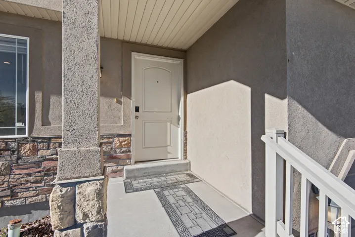 Covered entryway featuring a stone-accented facade, stucco siding, and white railing
