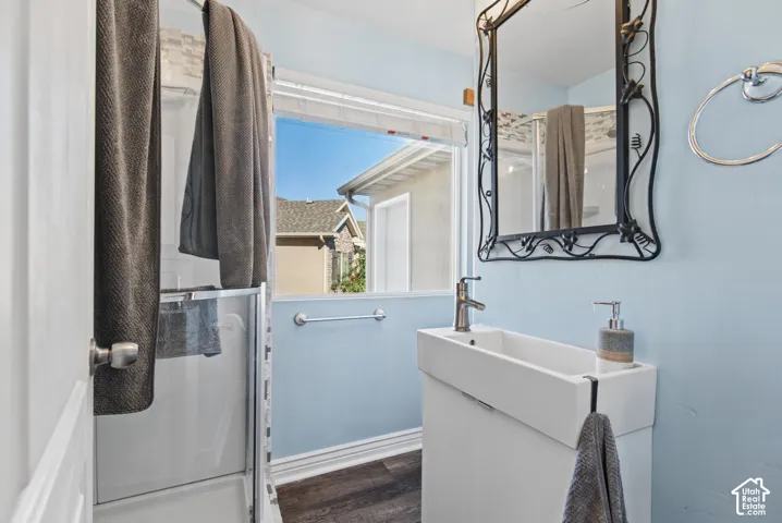 Bathroom featuring a white pedestal sink with a metal faucet, shower stall with sliding glass doors, dark wood-finish flooring, and a window with a mounted grab bar
