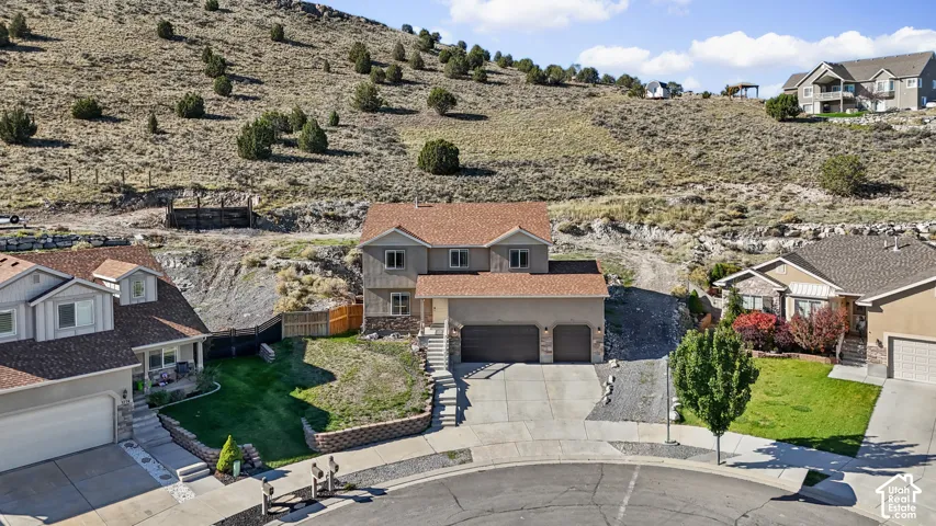 Two-story residence featuring a multi-tone stucco and stone exterior, shingle roofing, attached three-car garage, concrete driveway, and tiered stone retaining walls