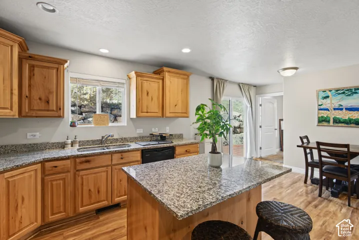 Kitchen featuring natural wood cabinetry, stone-patterned countertops, a central island, recessed lighting, and wood-finish flooring