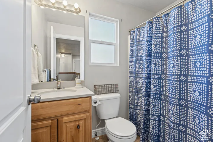 Bathroom featuring a wood-finish vanity with a composite countertop, integrated sink, wall-mounted light fixture, and a shower-tub combination