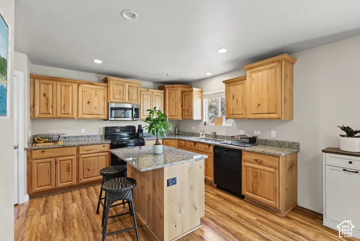 Kitchen featuring natural wood cabinetry, stone-surface countertops, central island, wood-finish flooring, and recessed lighting