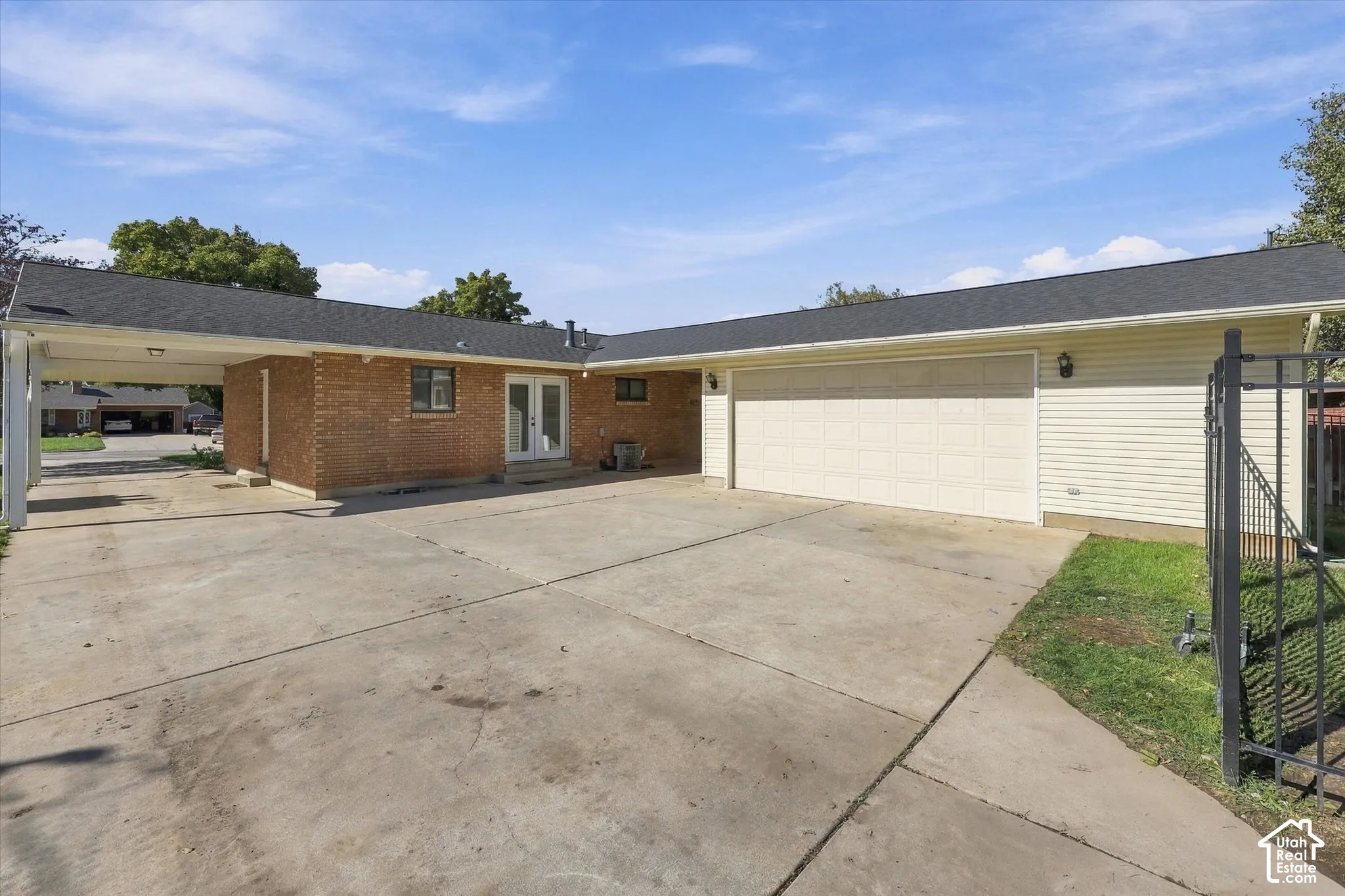 Exterior featuring brick and horizontal siding, an attached two-car garage, a covered carport, and metal perimeter fencing