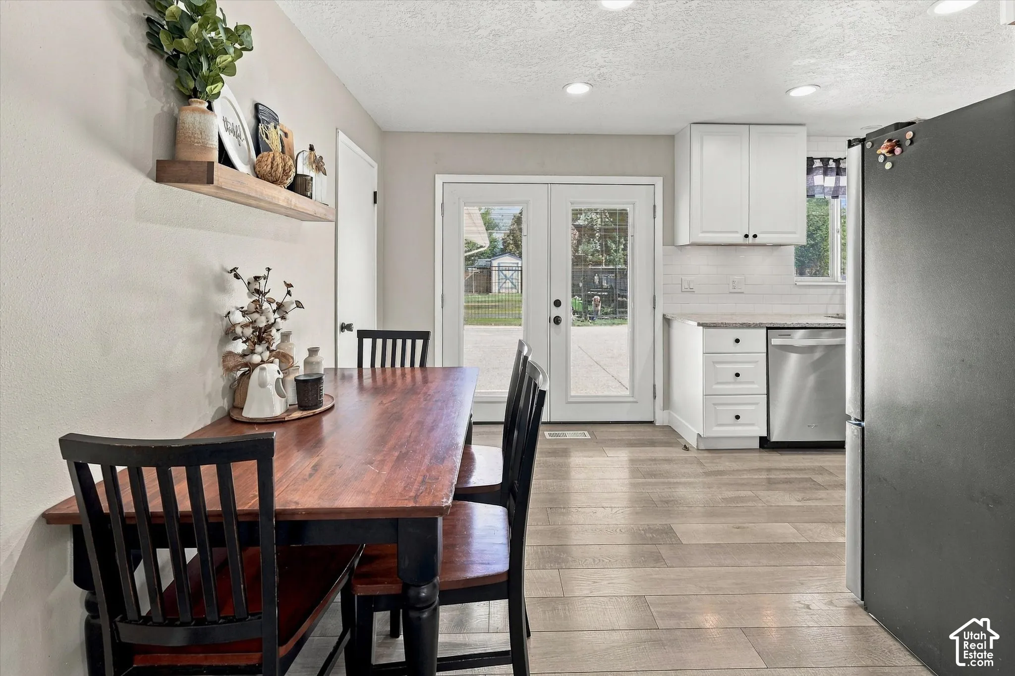 Kitchen and dining area featuring wood-finish flooring, white shaker-style cabinetry, stainless steel dishwasher, and double glass patio doors