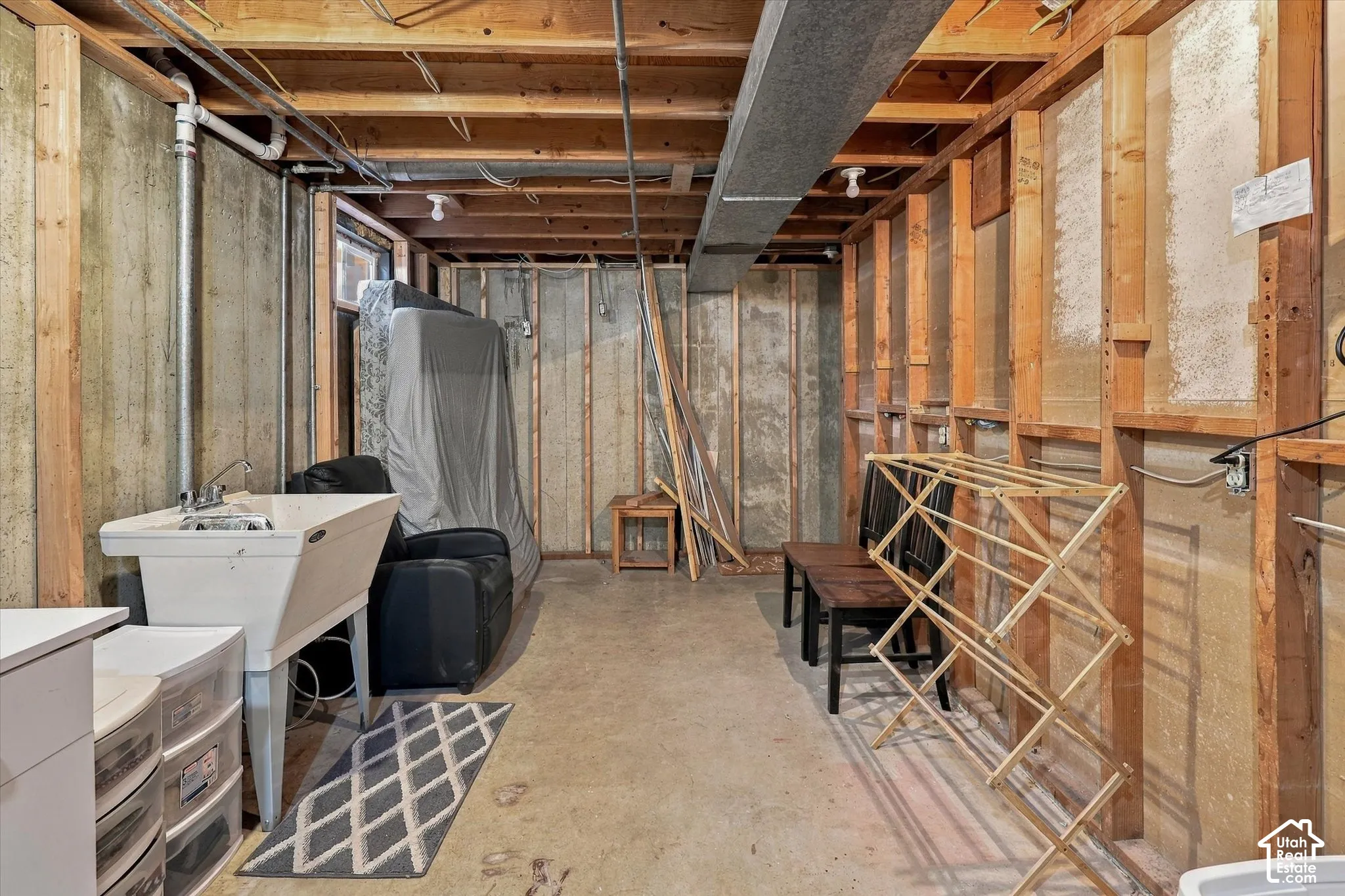 Unfinished utility area featuring exposed wood stud wall framing, concrete foundation walls, a concrete floor, and a utility sink