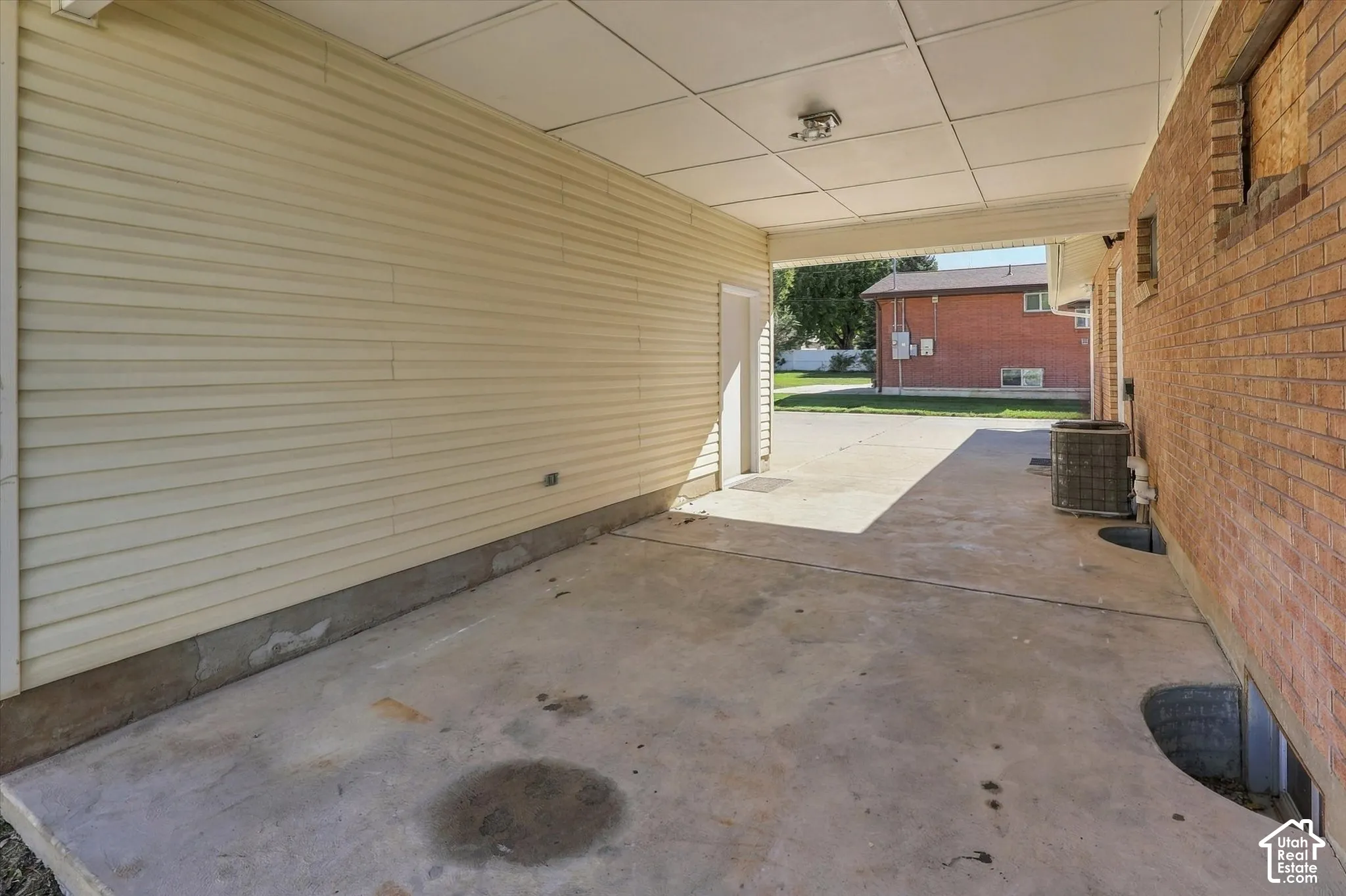 Covered carport featuring light-colored horizontal siding, a concrete floor, and brick exterior wall detailing